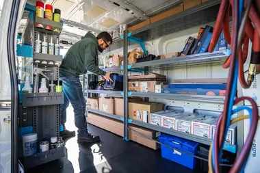 man organizing materials and work tools on an Adrian Steel shelf unit inside a van